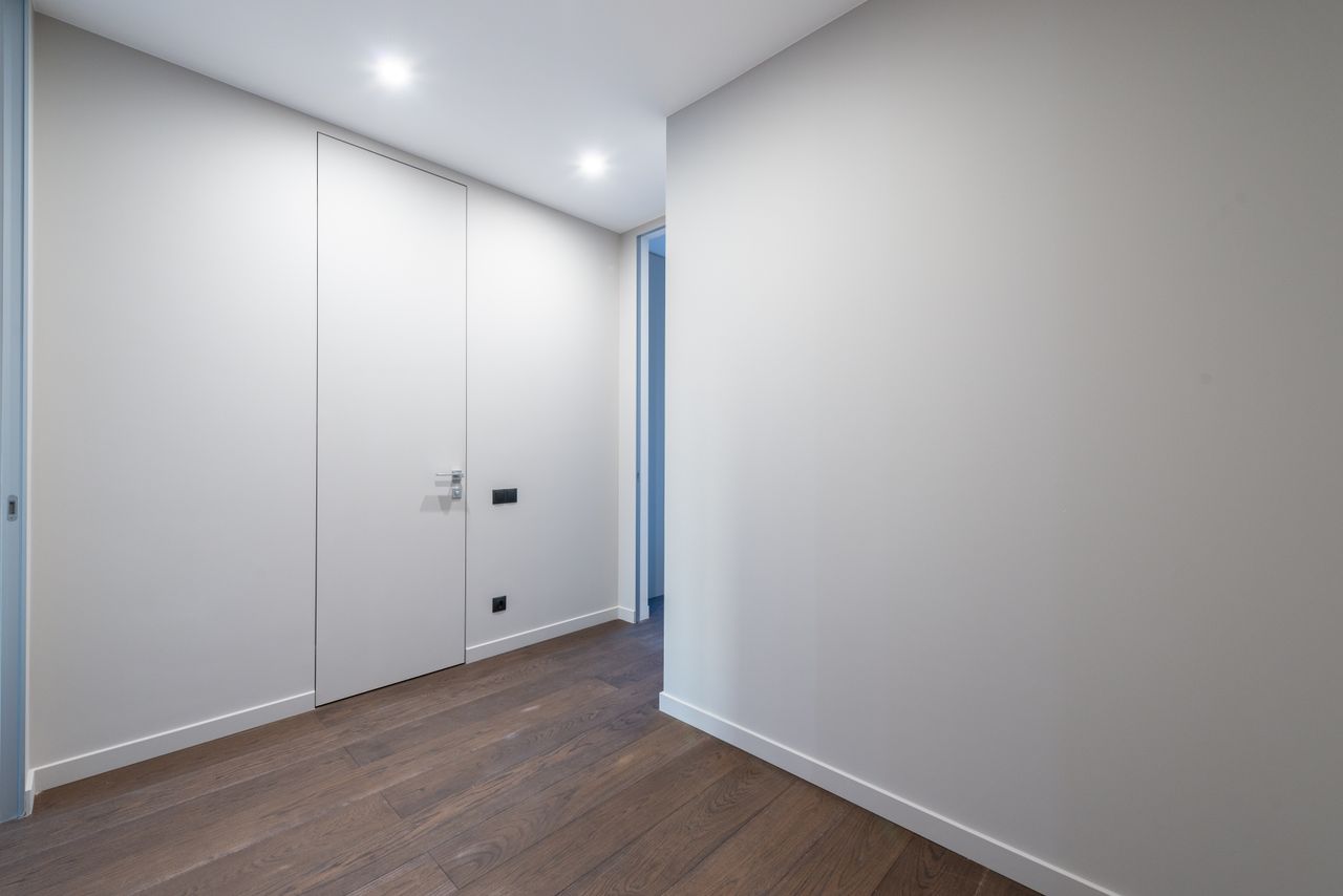 A minimalist indoor corridor featuring sleek doors and wooden flooring under bright lighting.